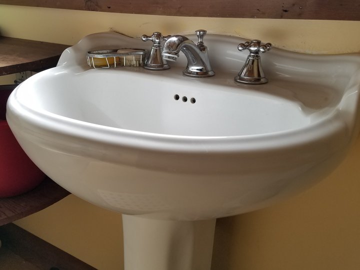 White pedestal bathroom basin with a chrome spout and two cross handles.