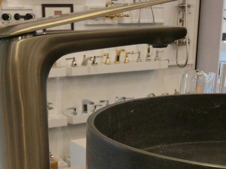 Close view of a bronze-tone faucet beside a dark round vessel basin.