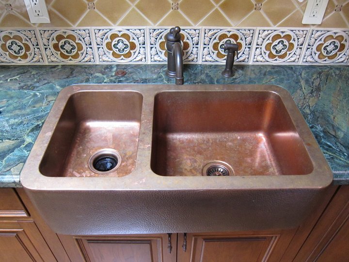Double-basin copper kitchen sink with a dark faucet and patterned tile backsplash.