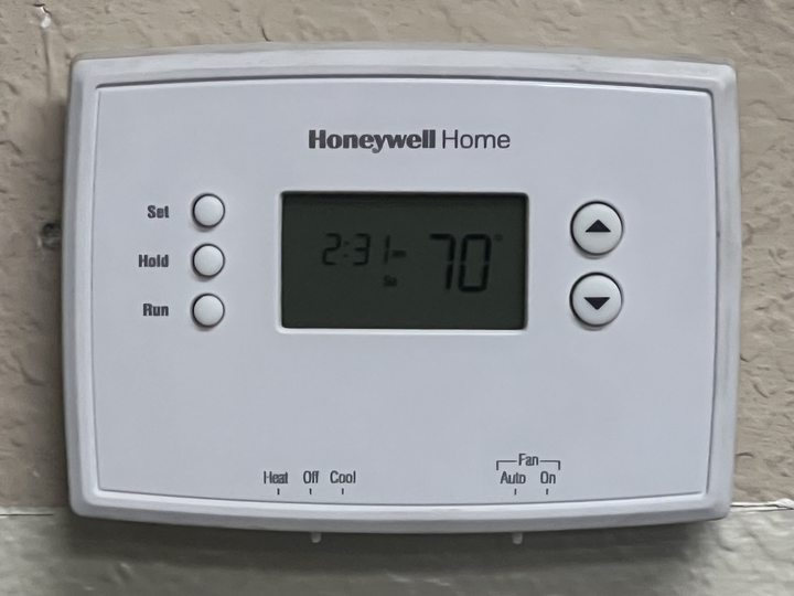 White wall thermostat with heating and cooling controls and a display reading 70 degrees