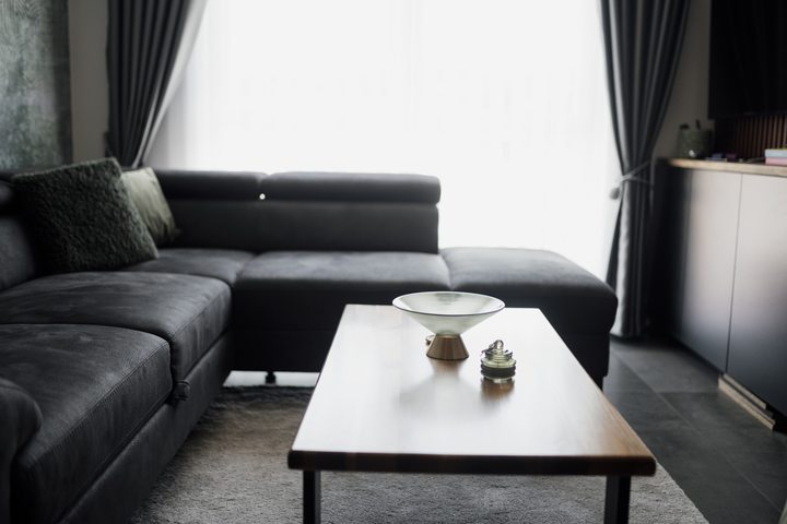 Gray sectional sofa and wooden coffee table beside a bright curtained window